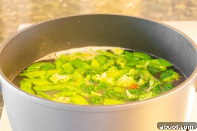A pot of boiling water containing vibrant broccoli florets, bright snow peas, and sliced carrots, gently blanching.