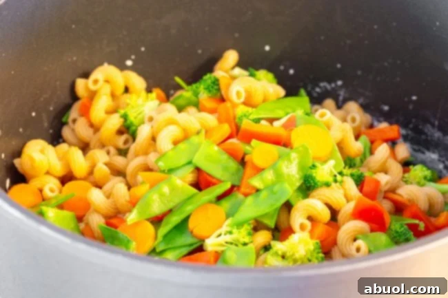 Drained pasta and blanched vegetables resting in a large pot after being rinsed, ready for the sauce.