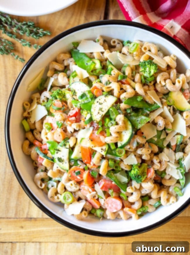 A top-down view of a serving bowl filled with creamy noodles, generously mixed with chopped zucchini, carrots, broccoli, and red peppers, elegantly garnished with shaved parmesan cheese.