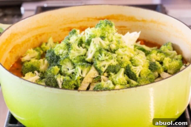 Adding Broccoli to Detox Soup Fresh broccoli florets being added to the simmering pot of vibrant detox chicken soup, rich with vegetables.