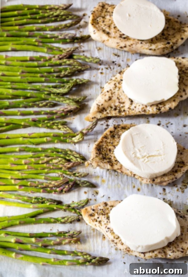 Sheet pan with partially baked chicken and mozzarella, alongside asparagus, ready for the oven.