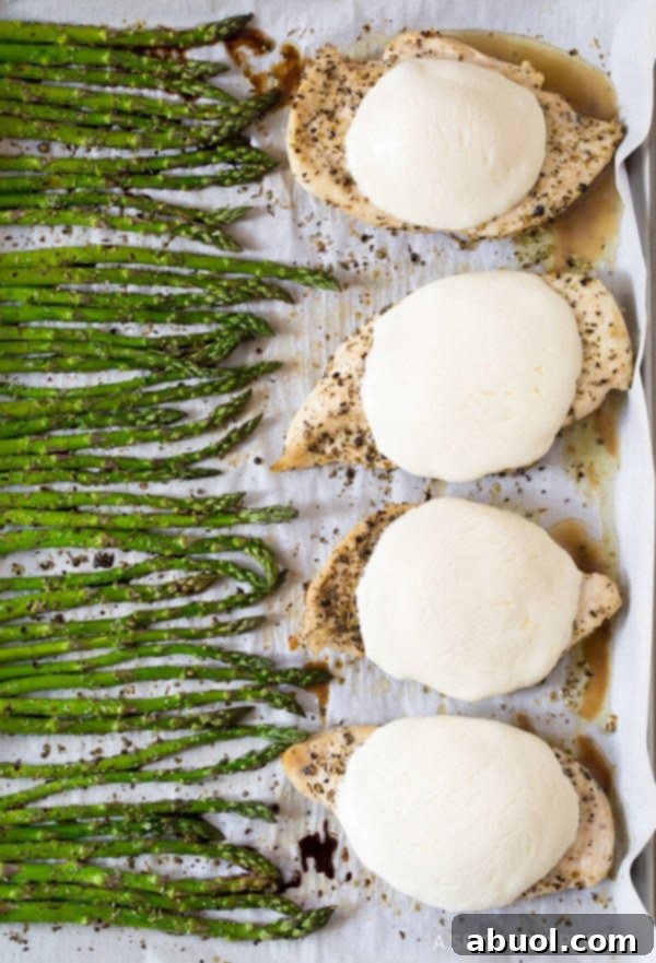 Sheet pan showcasing freshly baked bruschetta chicken with melted mozzarella and roasted asparagus.