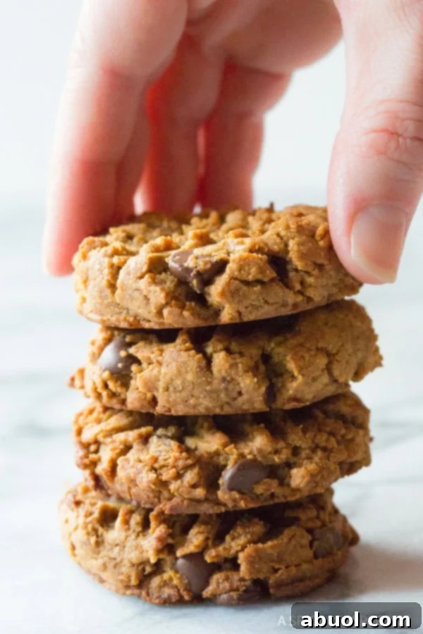 A hand reaching for the top cookie from a tempting stack of four freshly baked peanut butter chocolate chip cookies, highlighting their inviting texture.