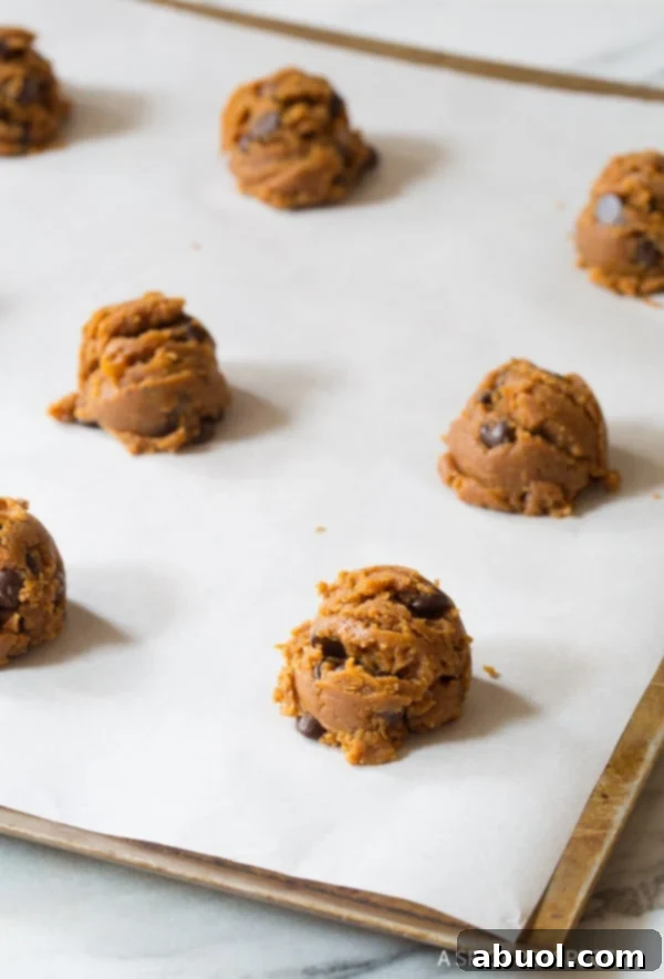 Neatly scooped rounds of raw cookie dough arranged on parchment paper on a baking sheet, spaced for optimal baking.