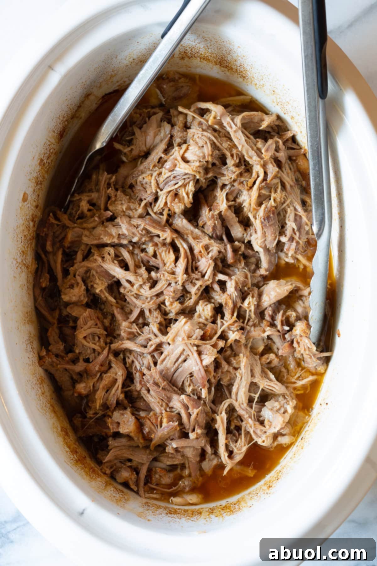 Shredded pork in the crockpot with metal tongs, ready to be served.