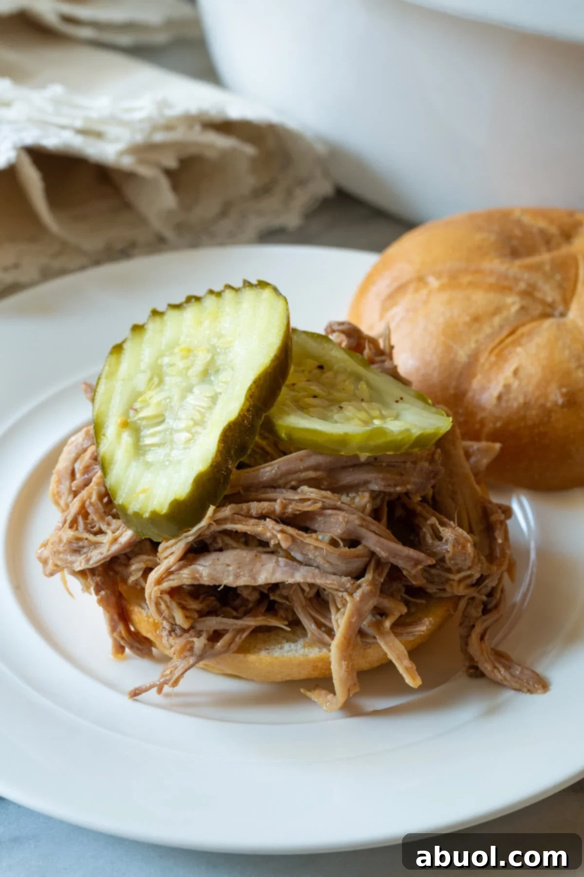 Shredded smoked pulled pork on a bun with pickles, a classic serving.