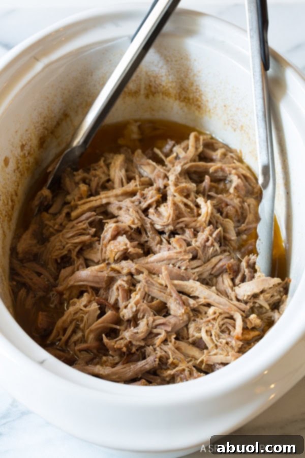 Shredded pork in the crockpot with metal tongs, showing the tender texture.