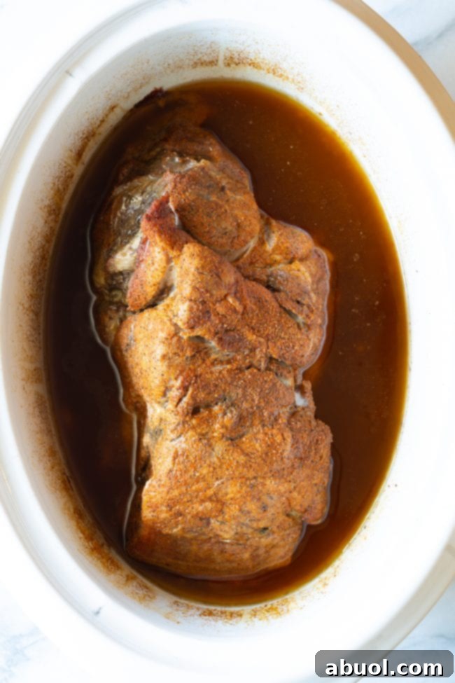 Cooked pork roast in a crock pot, tender and falling apart.