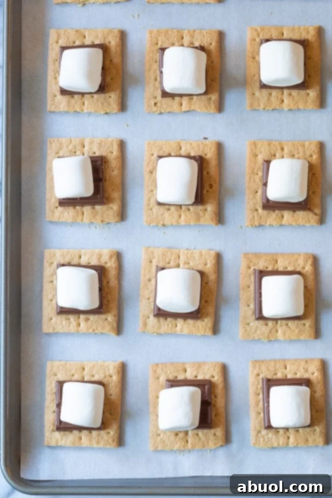 Oven Baked Smores Perfection 5 Overhead shot of graham cracker halves topped with chocolate squares and marshmallows, arranged on a baking sheet before broiling.
