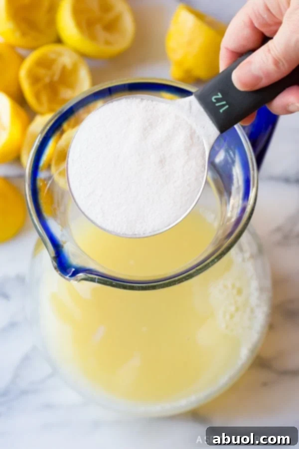 A hand carefully pouring powdered stevia into a pitcher of lemon juice.