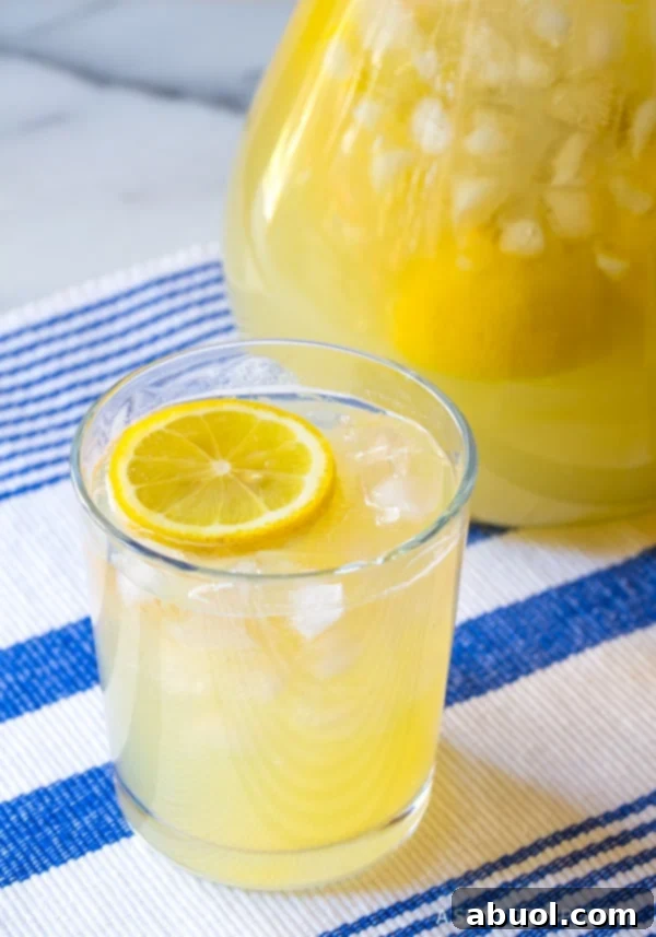 A tall glass of Best Stevia Lemonade, filled with ice and garnished with a lemon slice, against a bright background.