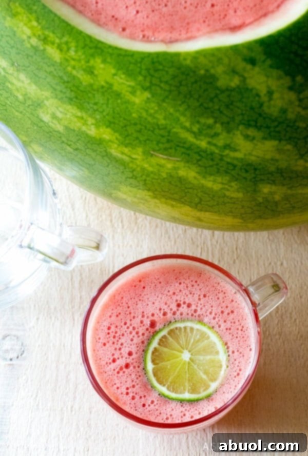 A top down view of rum punch in a glass with a lime slice next to the watermelon bowl.