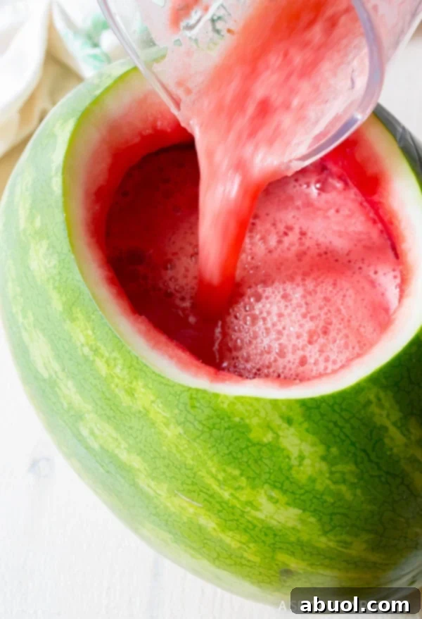 A blender pouring rum punch into the watermelon bowl.