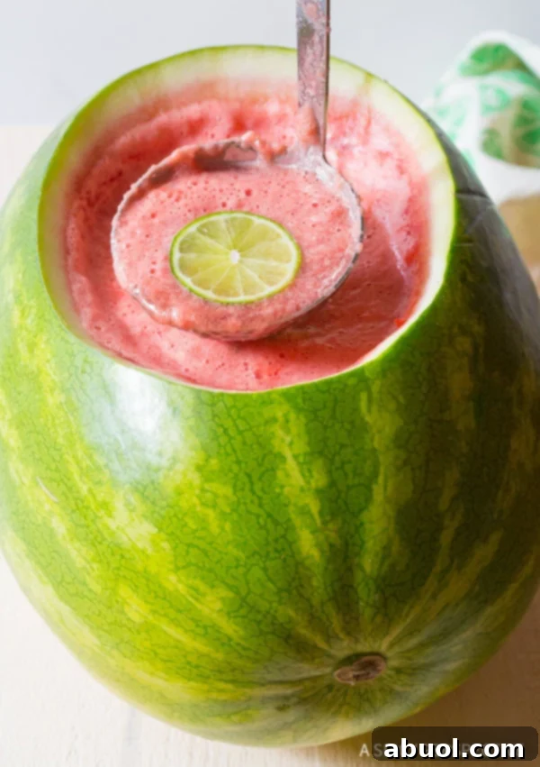 A punch ladle holding a serving of rum punch above the watermelon bowl.