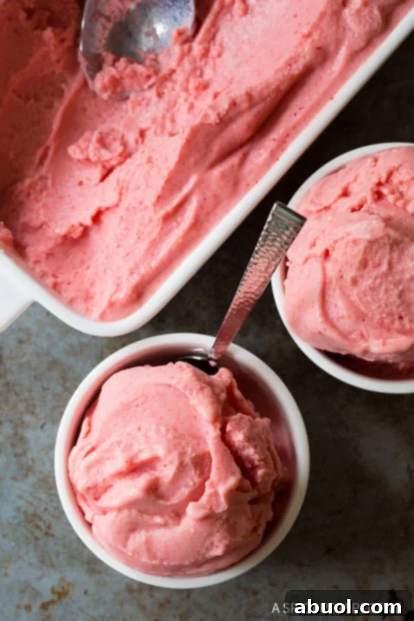 A top-down view showcasing a pristine white bowl filled with creamy strawberry pineapple sherbet, a metal spoon gently resting within.