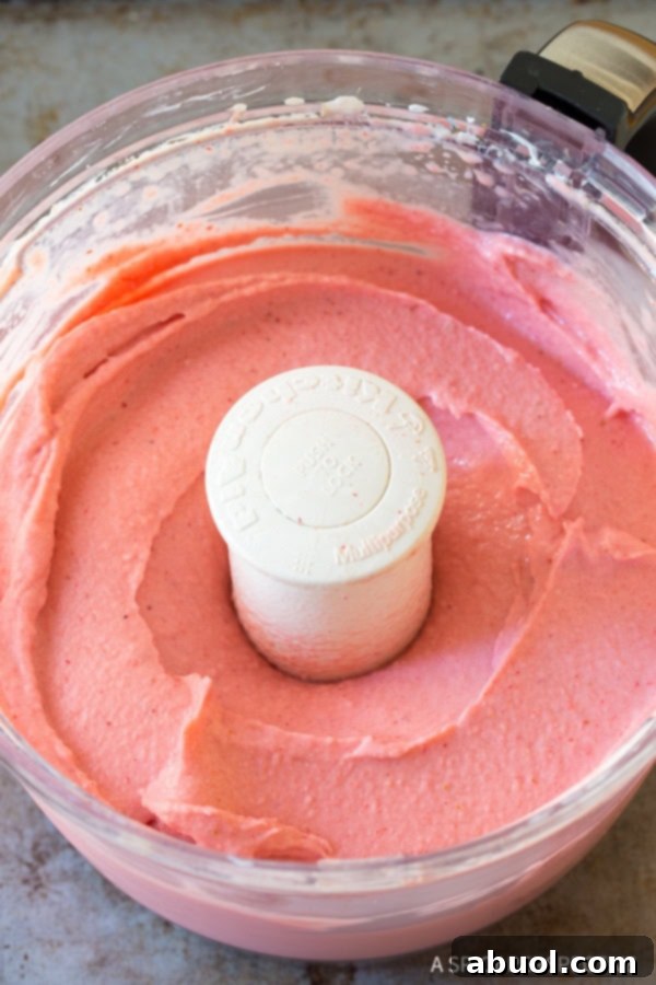 Smooth, creamy strawberry pineapple sherbet freshly blended in a food processor bowl, showcasing its perfect soft-serve texture.