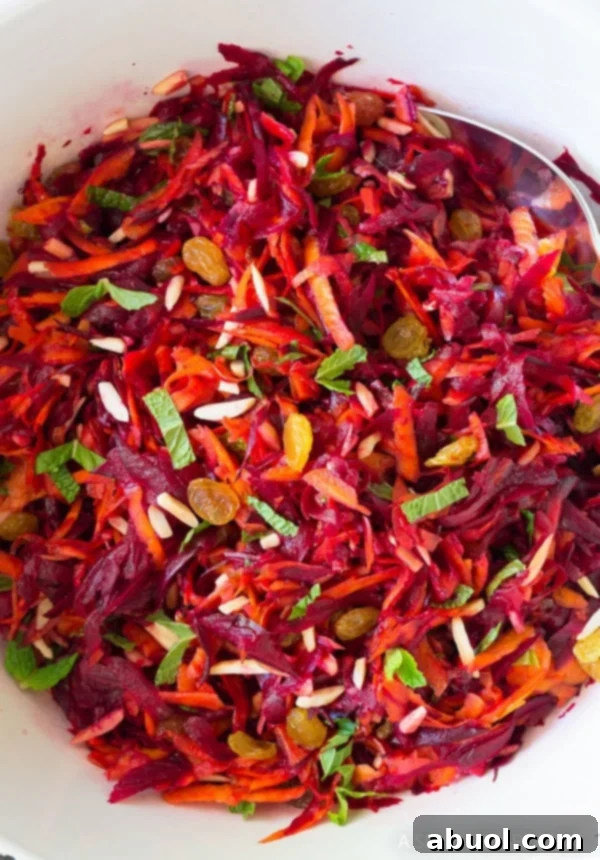 A serving dish filled with colorful carrot beet slaw, garnished with fresh mint leaves.