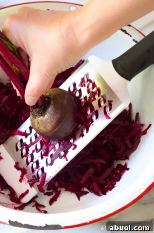 A hand grating raw beets into a mixing bowl.