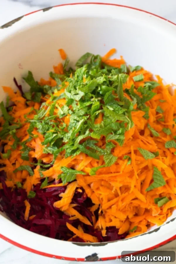 A large bowl packed with freshly shredded beets, carrots, and chopped mint.