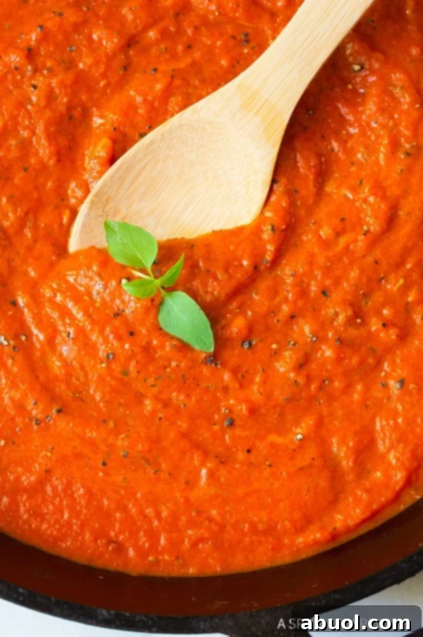 Roasted red pepper sauce with a wooden spoon and sprig of basil. 