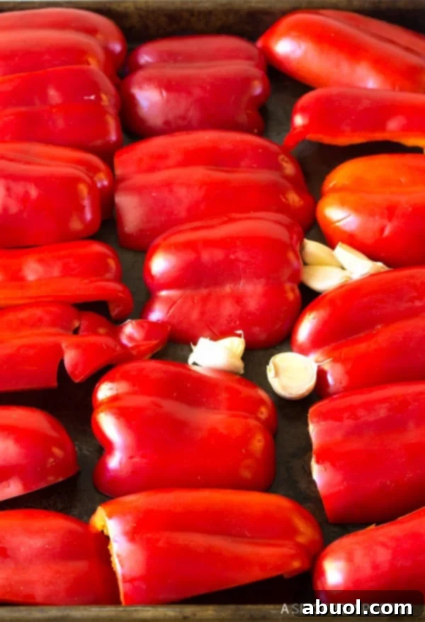 Red peppers and garlic cloves on a baking sheet. 