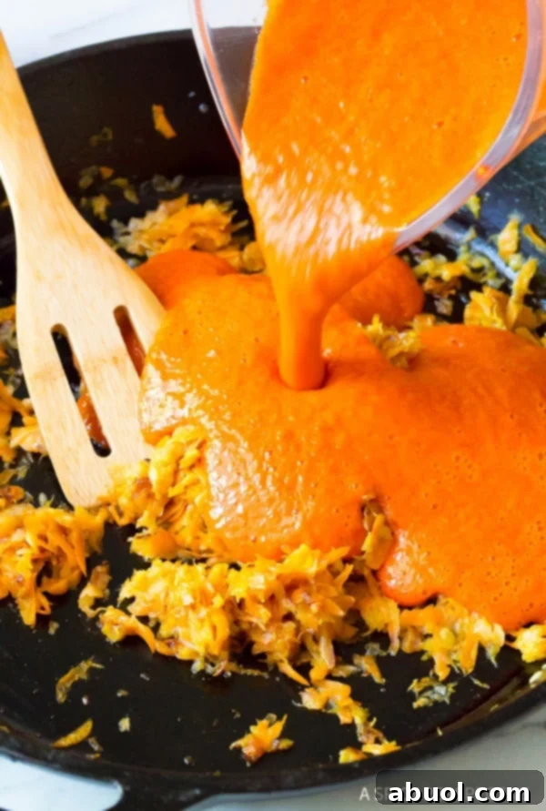 Pouring the blended red peppers into a pan with carrots and onions. 