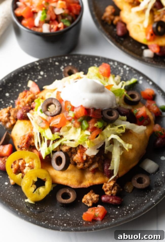 Navajo fry bread topped with ground beef and other taco toppings on a black plate, showcasing a hearty and flavorful Indian Taco.