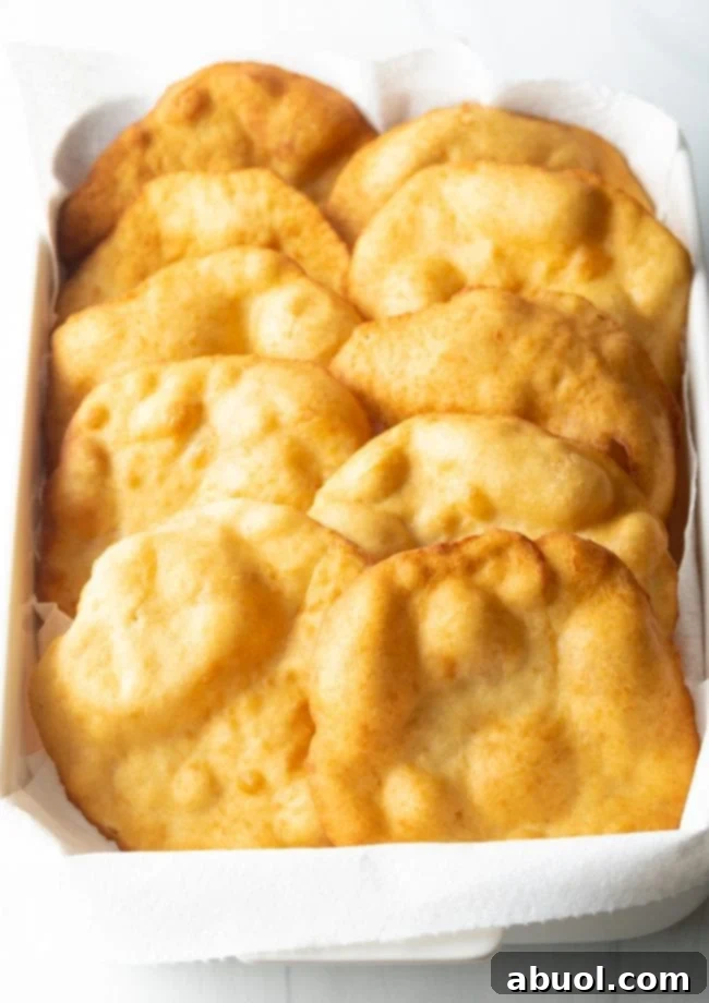 Freshly fried, golden-brown fry bread tortillas draining on paper towels in a baking dish.