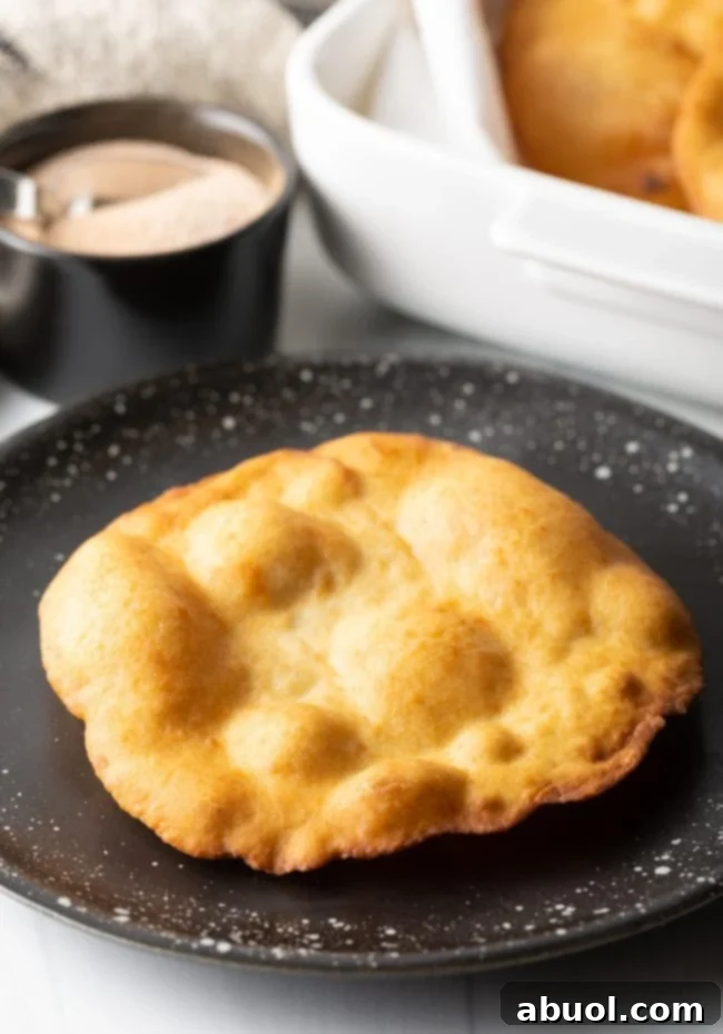 A perfectly crispy piece of fry bread resting on a black plate, golden and inviting.