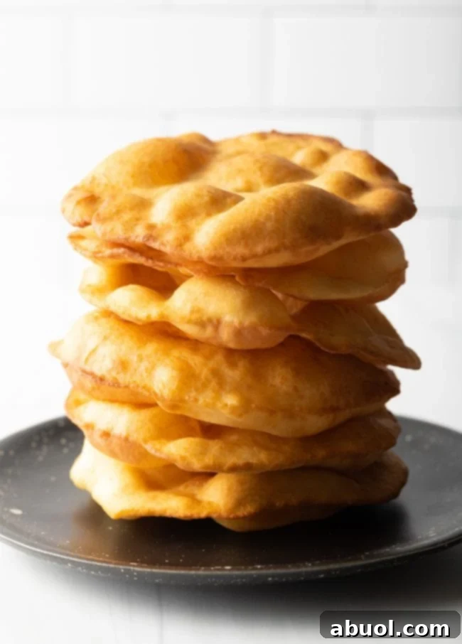 A large stack of golden-brown Navajo fry bread, ready to be enjoyed as a snack or part of a meal.