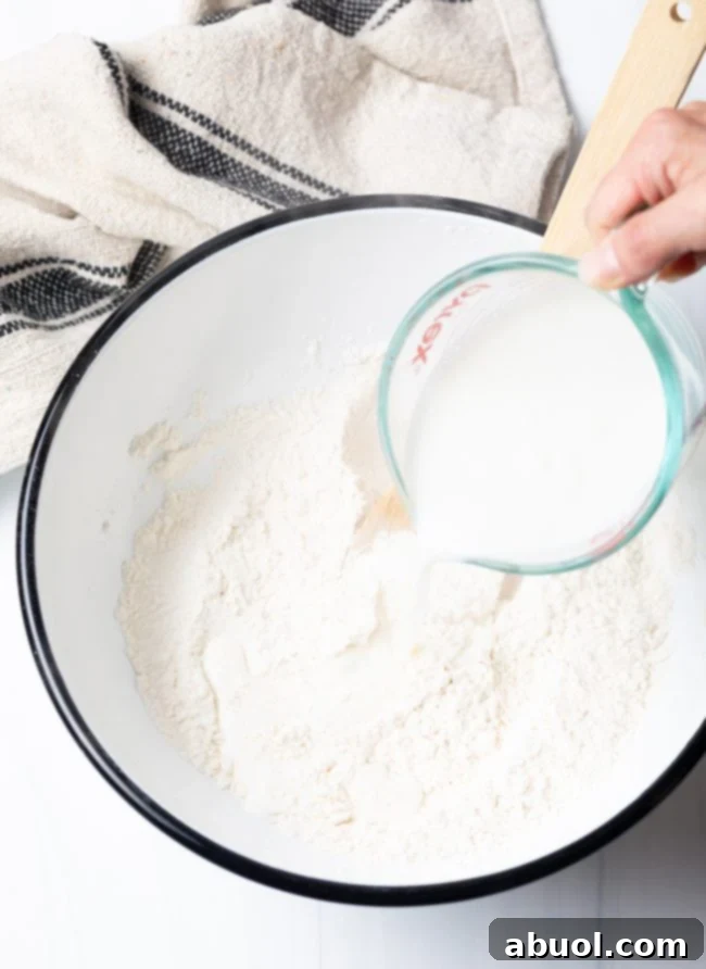 A hand pouring wet ingredients into a mixing bowl to combine with dry ingredients and form the dough.