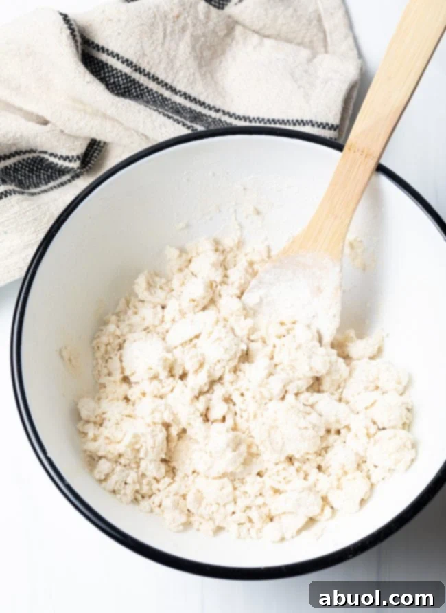 Navajo fry bread dough being mixed with a wooden spoon in a bowl, showcasing its developing consistency.