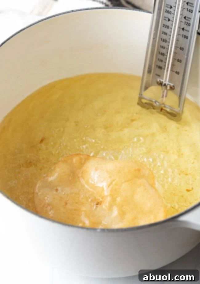 Tongs flipping a piece of fry bread in hot oil, showing its beautiful golden color.