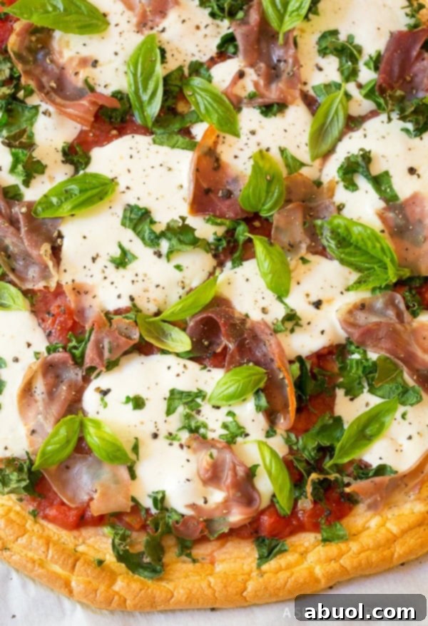 Close up shot of the vibrant toppings on a cloud bread pizza, featuring mozzarella, kale, and prosciutto.