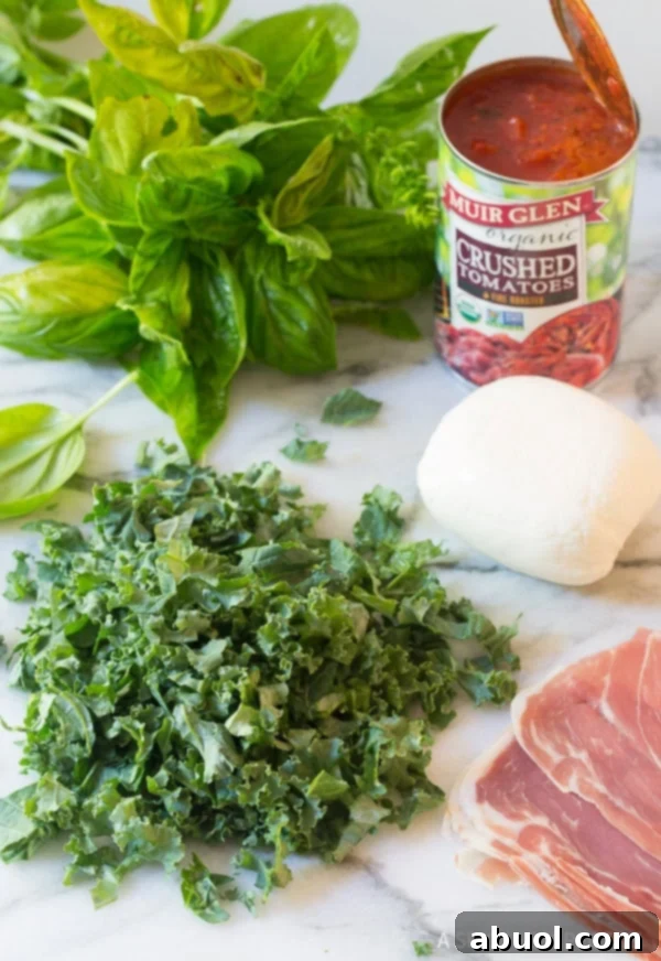 A selection of fresh ingredients laid out, including tomatoes, mozzarella, kale, prosciutto, and basil, ready for pizza assembly.