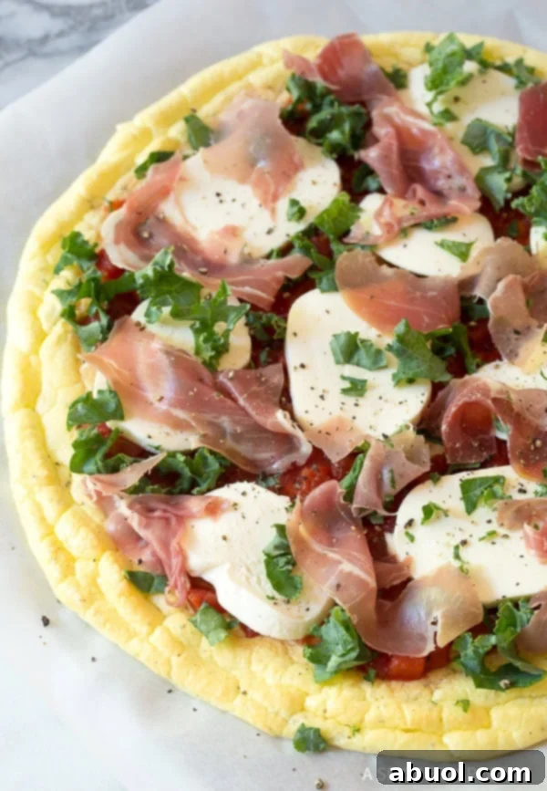An assembled cloud bread pizza, richly topped with sauce, mozzarella, kale, and prosciutto, awaiting its final bake.