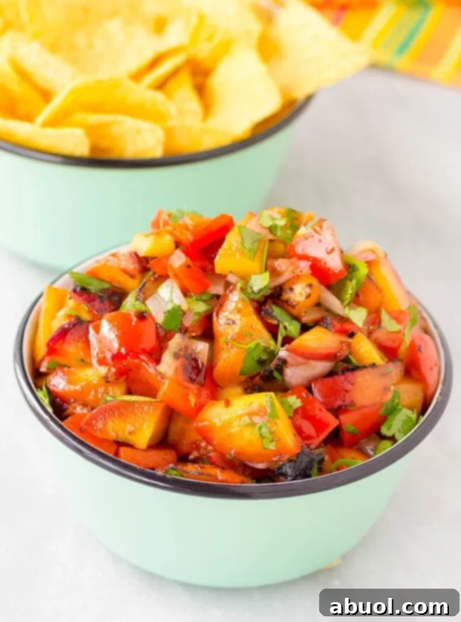 A beautiful bowl of grilled chipotle peach salsa, vibrant with fresh ingredients, served alongside a basket of crispy tortilla chips, inviting a delicious scoop.