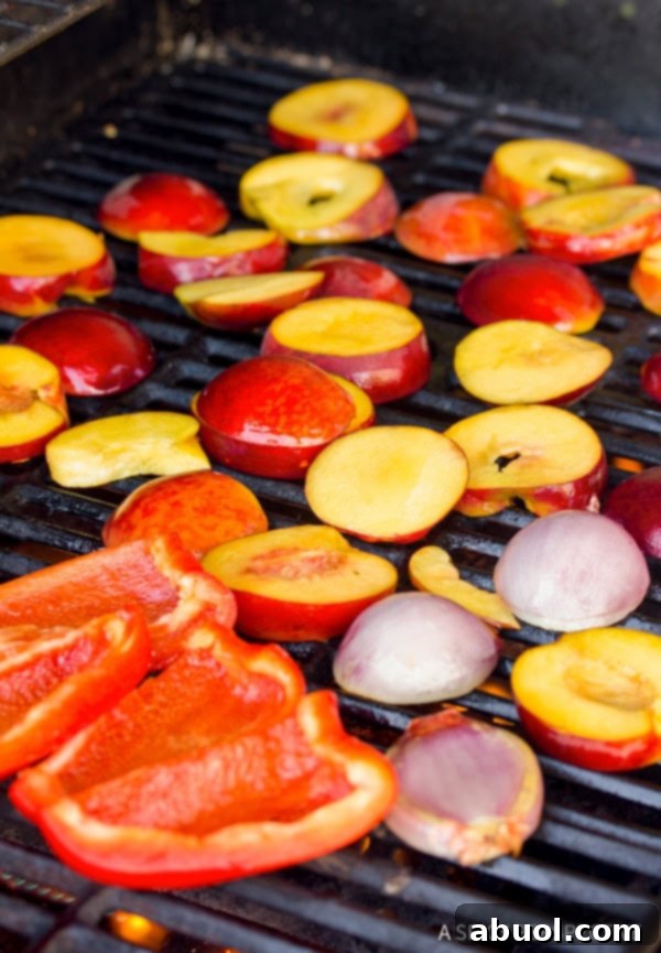 A close-up view of peaches, shallots, and red bell peppers grilling to perfection on an outdoor grill, showing appealing char marks.