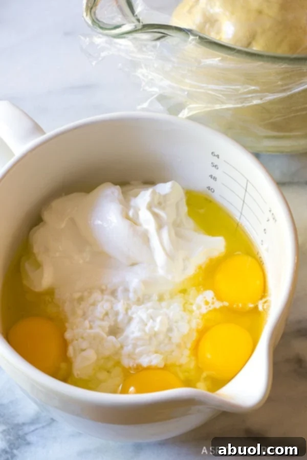 A close-up view of fresh cottage cheese, creamy sour cream, and beaten eggs being combined in a large mixing bowl, forming the luscious base for the Croatian Cheese Strukli filling.
