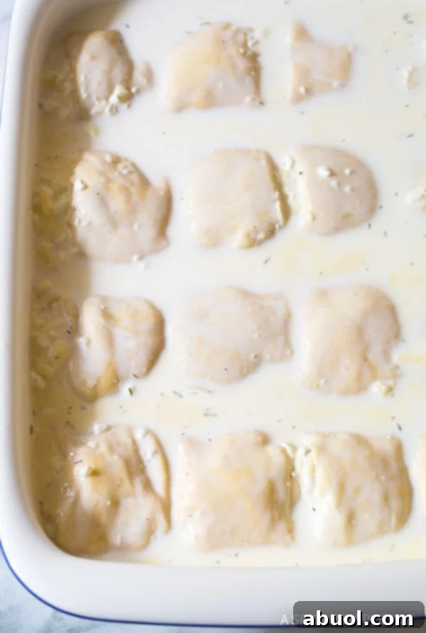 The assembled Croatian Cheese Strukli in a baking dish, glistening with half-and-half and topped with a generous layer of shredded cheese, perfectly poised before being baked to golden perfection.