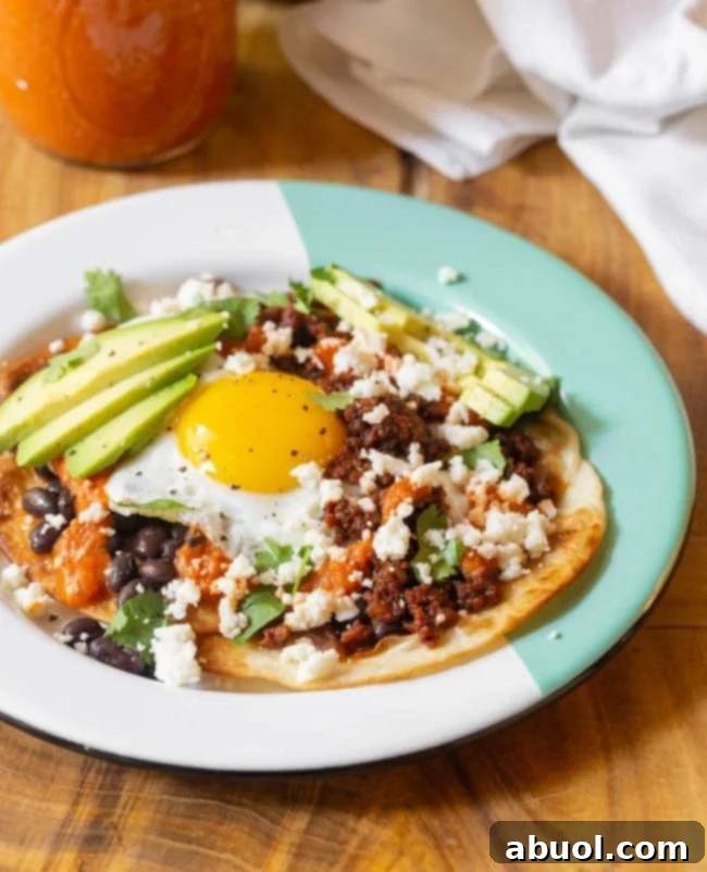 A beautifully composed plate of finished Huevos Rancheros, featuring sunny-side-up eggs, chorizo, black beans, avocado slices, and crumbled queso fresco, all ready to be enjoyed.