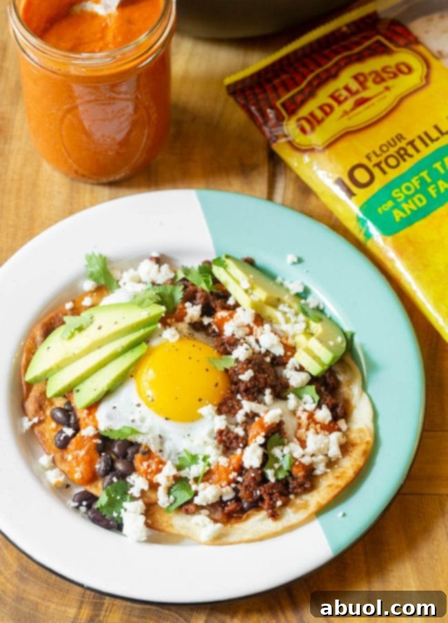 A beautifully plated Huevos Rancheros with a generous amount of ranchero sauce, accompanied by black beans, chorizo, and fresh avocado slices, ready to be enjoyed.