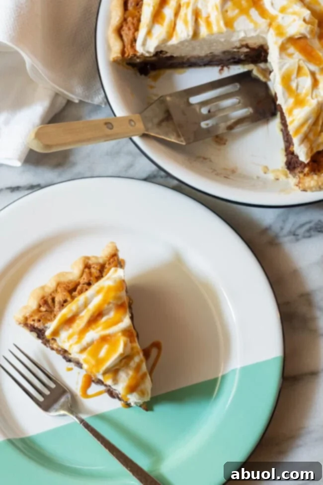 A slice of Kentucky Derby Pie adorned with swirls of salted caramel whipped cream on a decorative white and green plate.