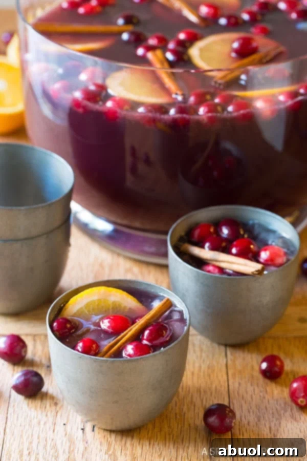 Holiday wine punch in a bowl with two silver glasses next to it filled with punch.