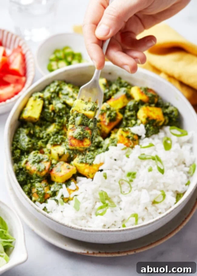 A hand with a fork picking up a bite of Saag Paneer, showing its creamy texture and a piece of paneer.