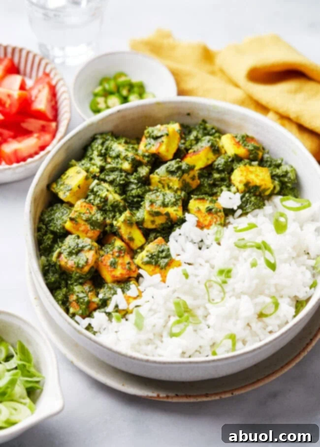 Saag paneer served alongside basmati rice in a bowl, with fresh ingredients in the background.