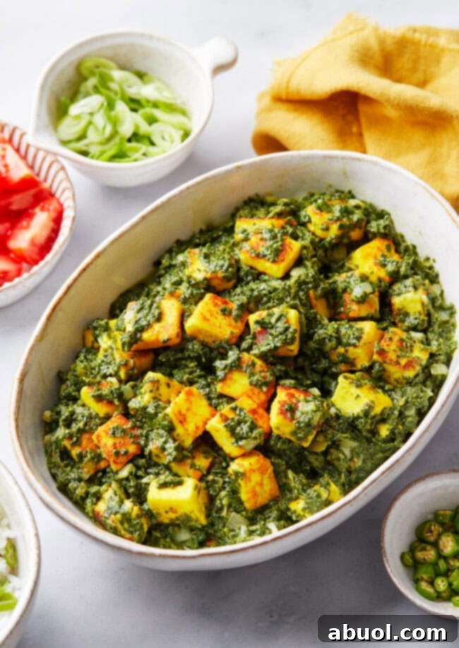 Saag paneer in a serving bowl with fresh ingredients like spinach, ginger, and spices surrounding it.
