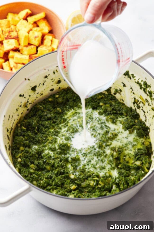 Coconut milk being added to the simmering spinach and spice mixture, adding creaminess.