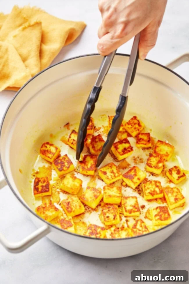 A hand searing paneer cubes in a hot pan, creating a golden crust.