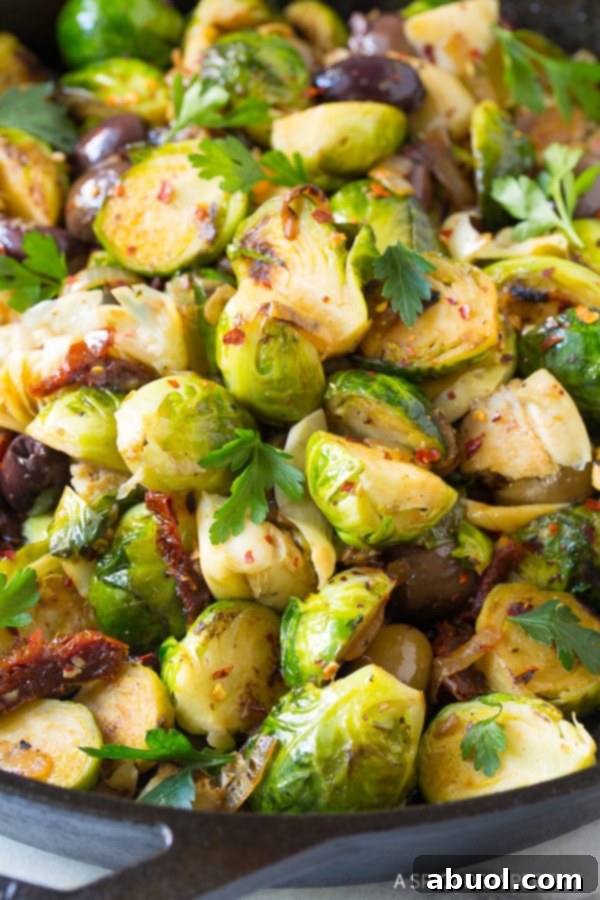 Close view of braised brussels sprouts with sun-dried tomatoes, greek olives, artichoke hearts and fresh chopped parsley.